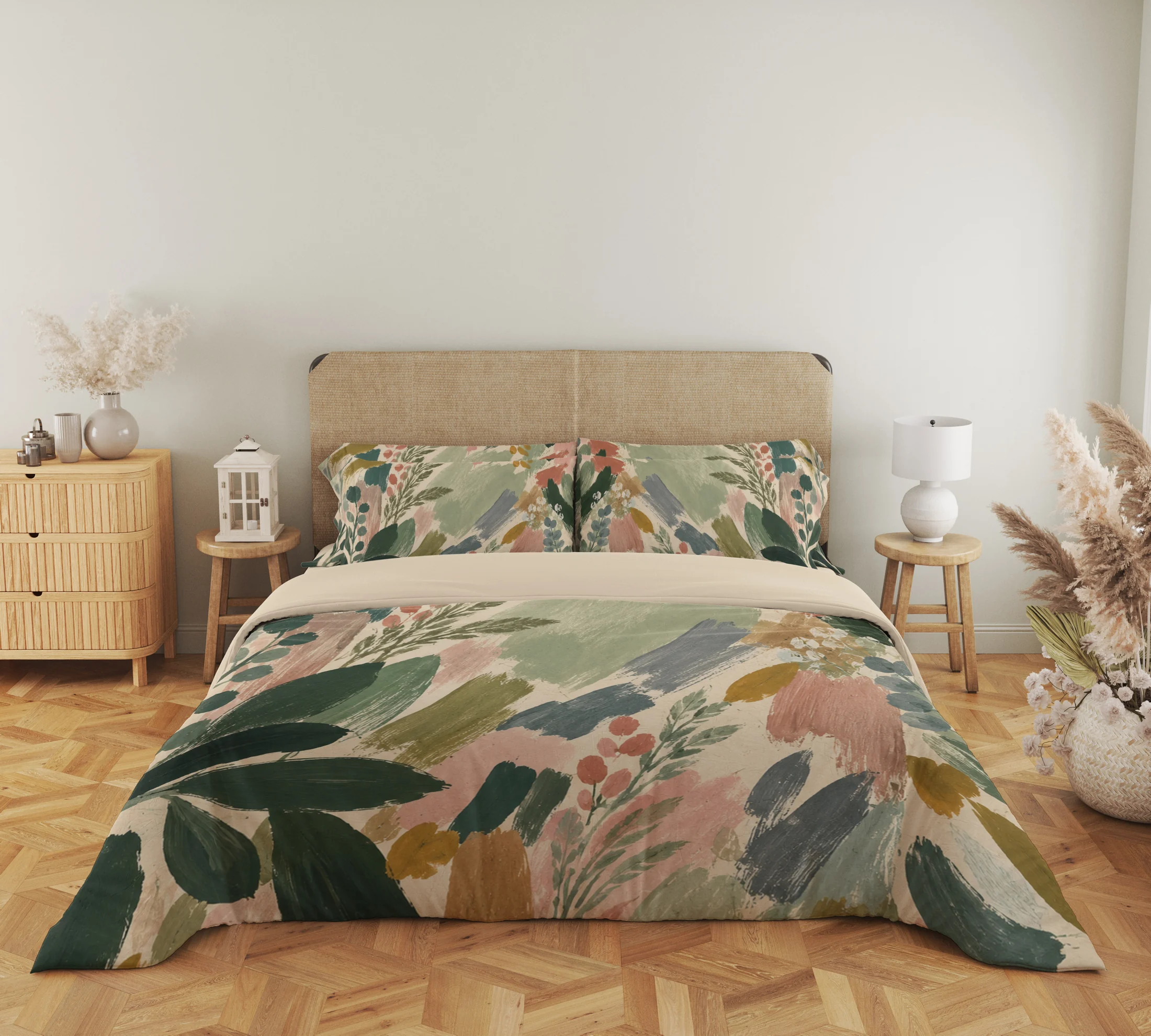 Close frontal view of a sage and blush brushstroke duvet with leafy sprigs, two printed pillows and a cream folded edge above a parquet floor.