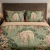 Front view of a sage duvet cover and matching pillows with hanging cream and dusty rose blossoms, dark branches and layered green leaves.