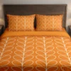 Bright orange bedding with fine ivory leaf loops across the duvet and pillows, shown from the front with a plain orange folded edge.