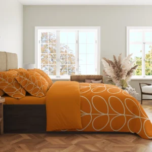 Side view of an orange duvet with ivory leaf outlines running over the hanging side and a solid orange fold near the patterned pillows.