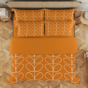 Overhead view of tangerine bedding showing rows of ivory loops on the pillows and large leaf stems below a wide orange fold.