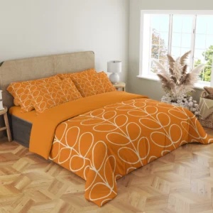 Angled view of an orange duvet with ivory paired leaves extending across the top and down the front corner, with matching pillows behind.