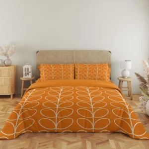 Full front view of tangerine-orange bedding with upright ivory leaf stems, a plain orange folded strip and coordinating patterned pillows.